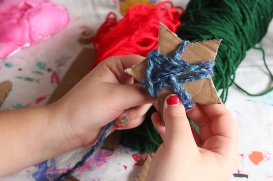 kid wrapping cardboard star in yarn