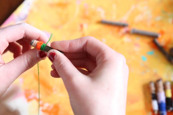 kid wrapping small twig with yarn or embroidery floss