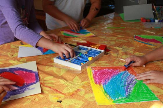 kids making base for scratch art with oil pastels