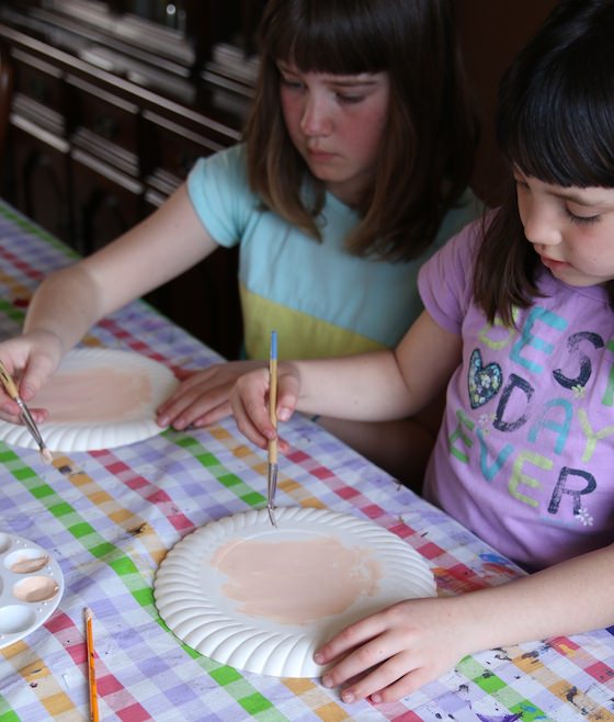 kids painting paper plates with skin-toned paint