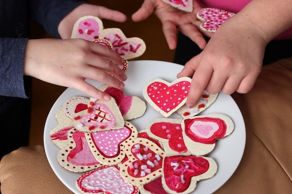 Kids putting heart shaped cardboard Valentines cookies on plate
