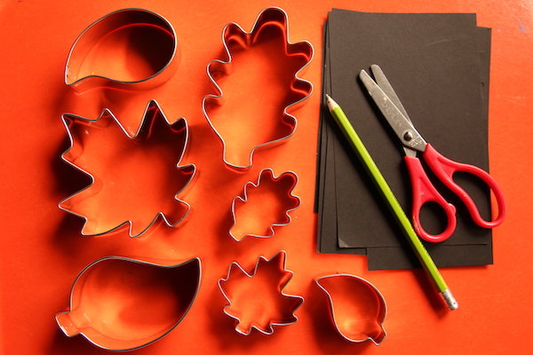 leaf cookie cutters, black paper, pencil, scissors on orange tray