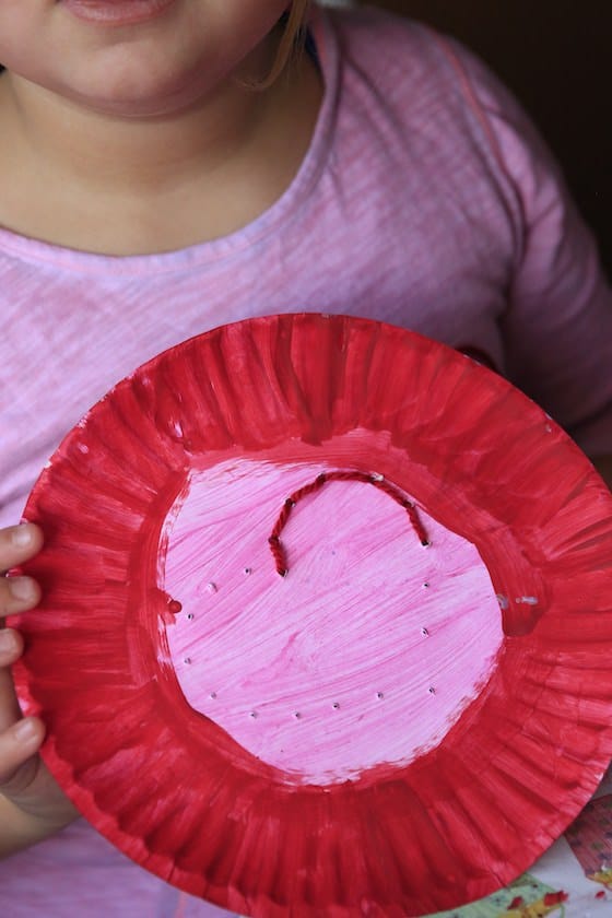 Child backstitching a heart onto a paper plate