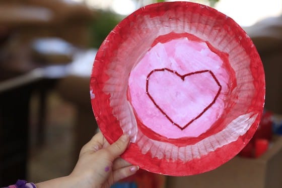 Child holding up red and pink paper plate