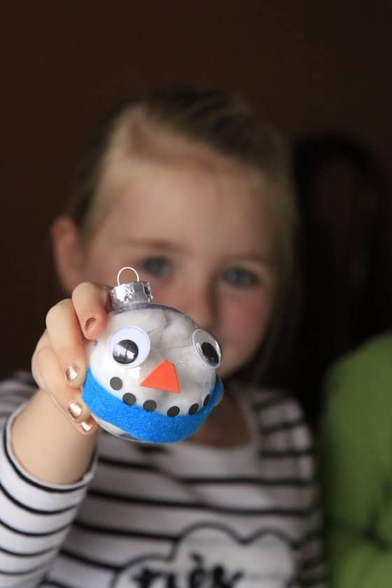 Girl holding out finished snowman ornament with blue scarf