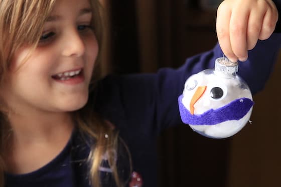 Child holding up finished snowman ornament with purple scarf