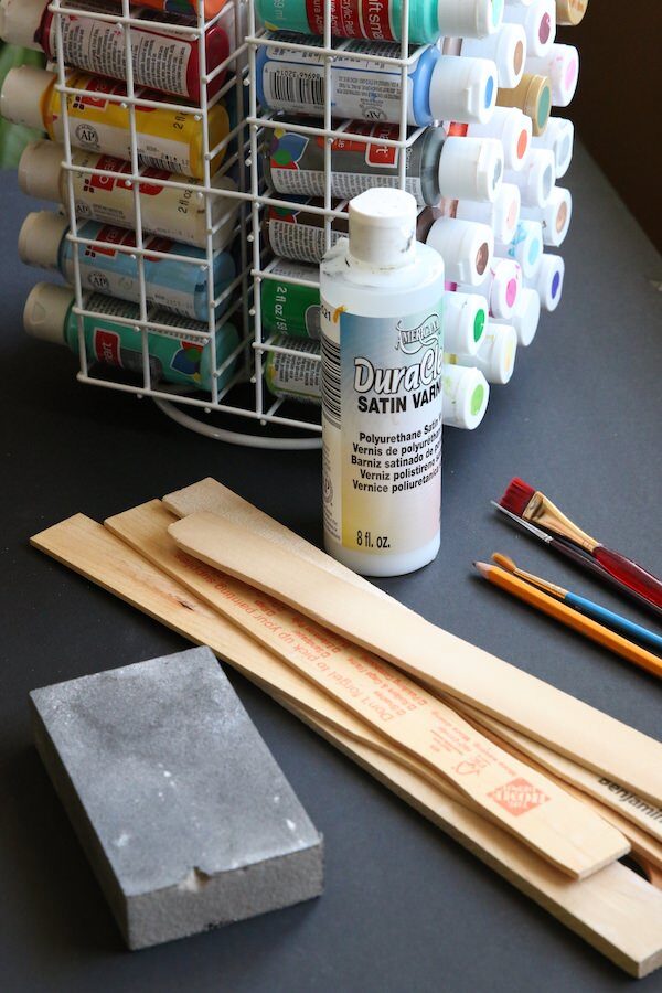 Paint sticks, paint, paint brushes, sanding block, varnish