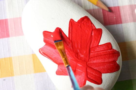 Painting a red maple leaf on a beach rock