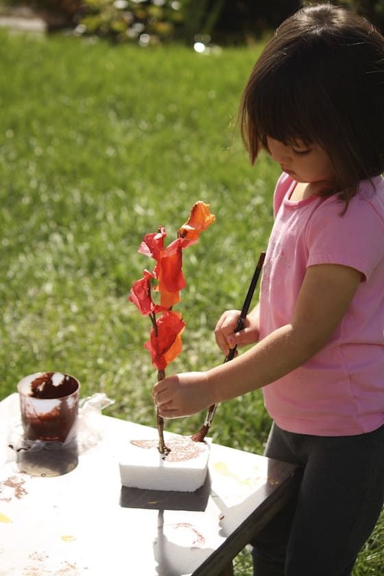 preschooler gluing red tissue paper to twig