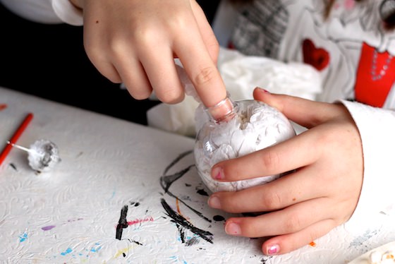 child filling clear ornament with white tissue paper