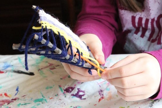 girl weaving on 3 pronged stick