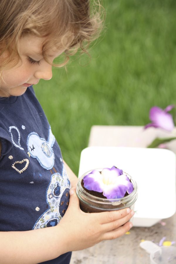 child holding artificial flower in glass jar of coffee grounds