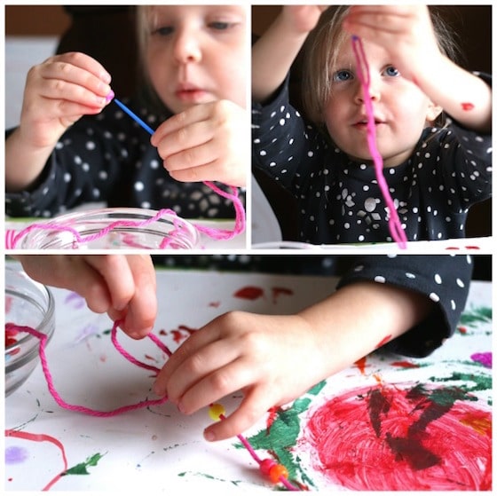 toddler stringing beads onto pink yarn