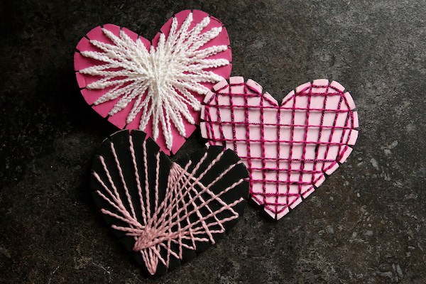 3 painted cardboard hearts strung with fine yarn.